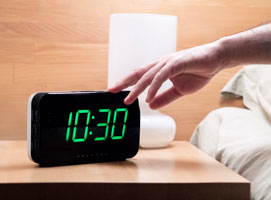 young man in bed reaching to turn alarm clock off at 10.30 a.m.